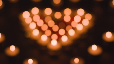 Defocused-Shot-Of-Romantic-Red-And-White-Candles-In-the-Shape-Of-A-Heart-On-Black-Background